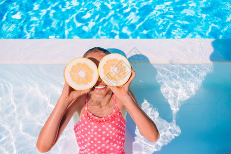 幸福肖像吃游泳池的小女孩有乐趣姑娘用柠檬眼罩着睛就在背景游泳池旁的一对面图片