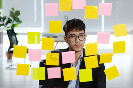 在室内公司提醒年轻的青亚洲商人在办公室阅读粘贴笔记时进行思考企业集广益为商业概念的成功规划创意构想思图片