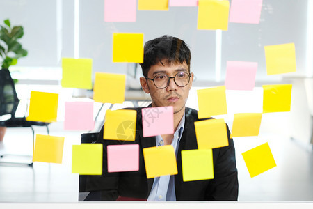 男人年轻的青亚洲商人在阅读办公室的粘贴笔记时思考商业大脑集思广益创造规划思想使商业概念成功工作解决方案图片
