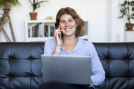 一种在线的身着蓝衬衫企业家妇女在沙发上用笔记本电脑工作网络图片