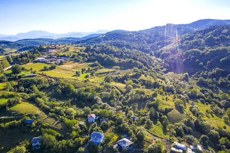 丘陵森林爬坡道无人驾驶飞机从空中观察美丽的山丘房屋和树木以及太阳耀斑的照片图片