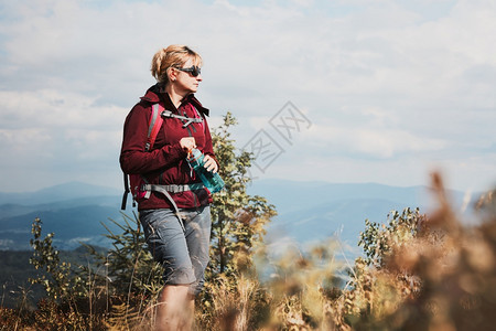 穿着背包在山上徒步旅行的女子在与自然相近的地方渡暑假妇女走在山顶上仰慕地风景全拿着瓶装水的子户外冒险远足图片