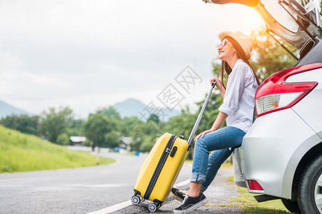 亚洲妇女在与黄行李同的路上度过周末女孩在汽车后背上放松有道路背景公旅行和假期概念人们的生活方式和交通路途快乐的开支趣背景图片