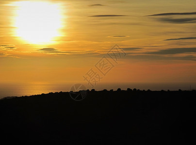 海面上日落前方有沿海山丘后在面上日落黄昏美丽的天气图片