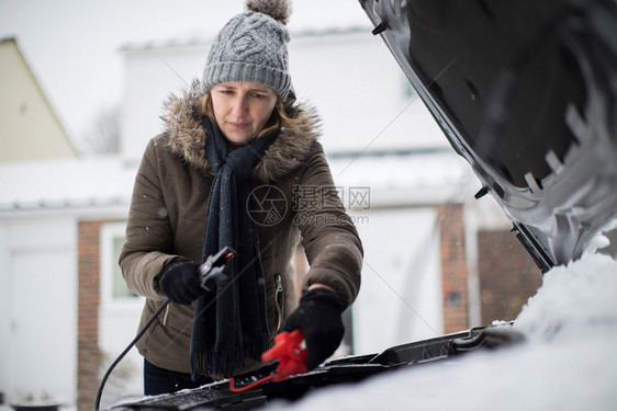 雪天在汽车电池上使用跳跃缆的妇女车库人们户外图片