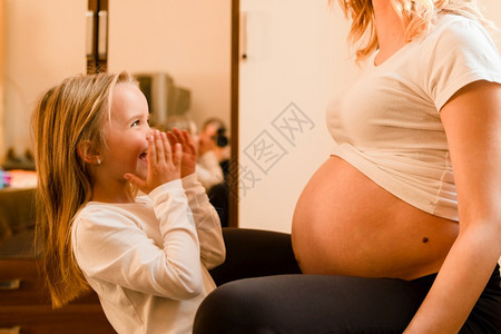 生活美丽的在家小女孩站孕妇母亲旁边站着等待小兄弟或妹出生而兴奋地等待着她出生新的图片