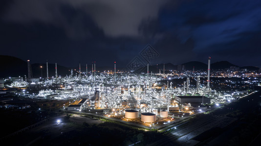 商业汽油夜间在泰国炼油区工厂使用不锈油管的轮和气罐车灯光模糊蓝天背景空中观察图片