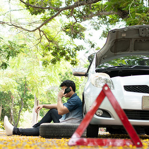 打电话技术为了亚洲男子坐在汽车旁边街头汽车故障后使用移动电话求救车辆发动机问题概念或事故以及专业技工的紧急帮助亚洲男子坐在汽车旁图片