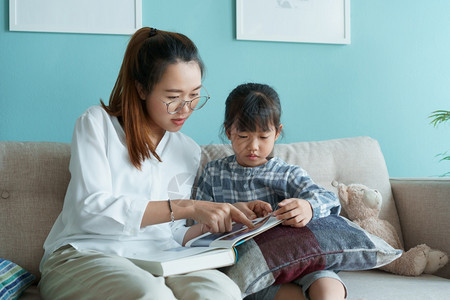 亚洲家庭与母亲和女儿一起读书的亚裔家庭在早晨坐沙发上客厅的教育保持韩国图片