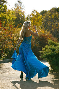 身着优雅蓝色礼服的金发美丽年轻女子自然孩树图片