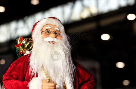 数字圣诞节毛皮穿着红色大衣装饰的玩具圣诞老人背着一包礼物在夜市背景下微笑穿过夜间城市着红皮外套在夜市里行走笑着过夜晚城市图片