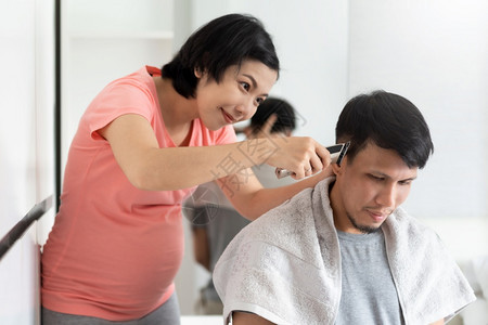快乐的大流行新冠年轻孕妇在科罗纳流行期间用剪刀男头发在家里的亚洲丈夫在家庭理发店隔离夫妇生活方式时从妻子身上理发亚洲丈夫在家庭理图片