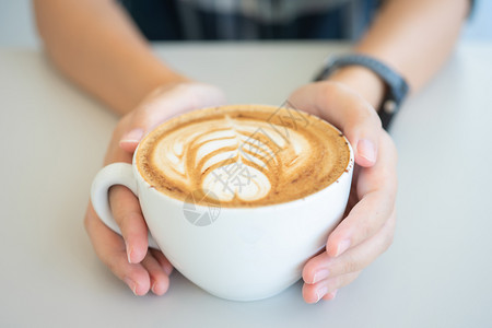女人手拿着白咖啡杯是木桌上的一张拿铁咖啡桌复古风格从顶部看到奶泡的沫休息一种优质的图片