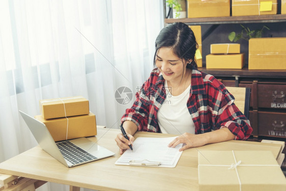 微笑商业盒子女检查库存商品供应包裹运输使用文件清单亚洲女在家办公创业小企在线家亚洲女使用平板电脑检查在线订单图片