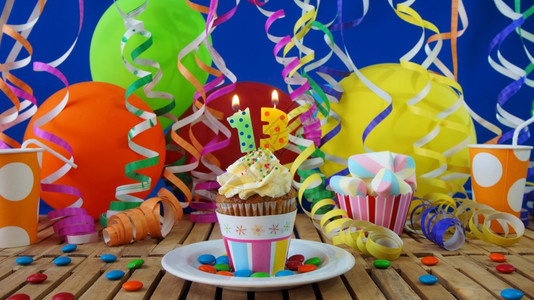 生日13小纸杯蛋糕在质朴的木桌上燃烧着蜡烛背景是五颜六色的气球塑料杯和糖果背景是蓝色的派对墙背景甜点喜庆的今天图片