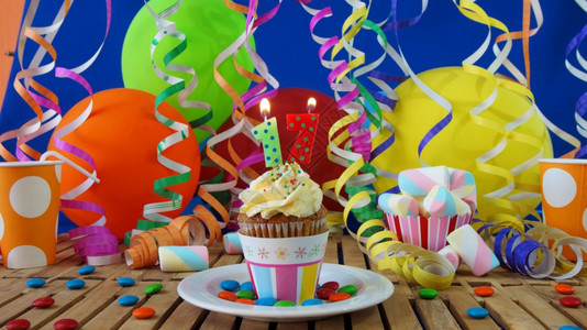 17岁生日小蛋糕在质朴的木桌上燃烧着蜡烛背景是五颜六色的气球塑料杯和糖果背景是蓝色的派对墙背景火家庆典图片