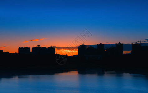 市中心夜间城景观高楼建筑在日落背景下的轮廓反映于与湖之夜城风景中发光的黄色图片