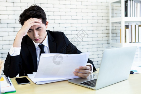 坏的危机精神紧张商人从事笔记本电脑工作在商业损失后头痛在办公室背景中成人图片
