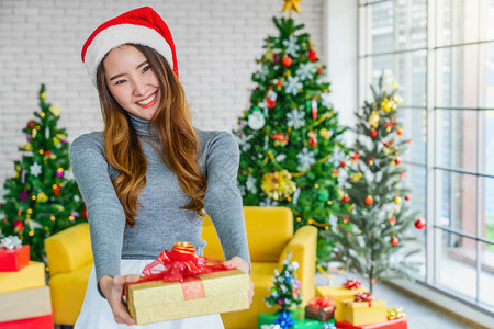 愉快身穿彩色红毛衣戴帽子并将礼物盒送给他人用于庆祝圣诞快乐亚洲人或室内聚会Xma和新年概念a纪念日沙发树木图片