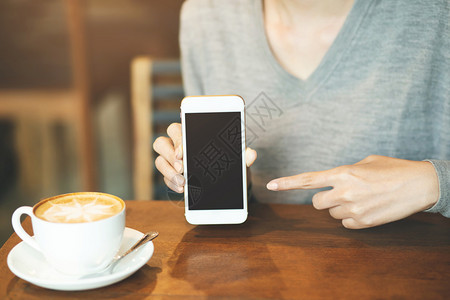 木制的空白桌子妇女在咖啡店喝时手握移动智能电话用空白桌面屏幕和手指触摸的头在咖啡店里喝图片