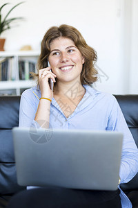 身着蓝衬衫的企业家妇女在沙发上用笔记本电脑工作坐着青少年无线上网图片