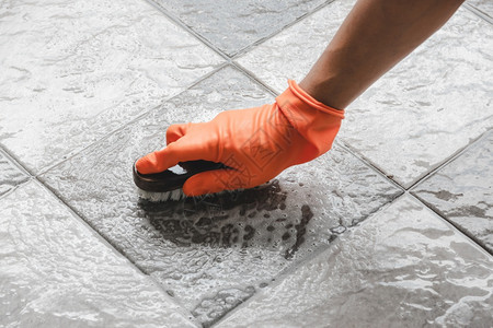 转变戴橙色橡皮手套的人用来在瓷砖地板上改装洗涤剂手动的保护图片