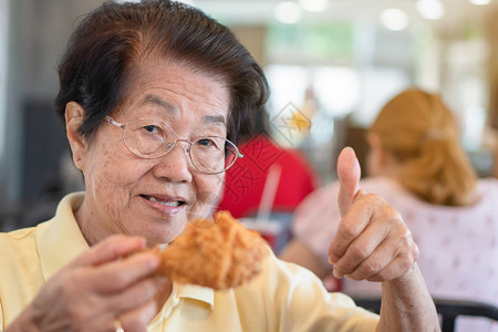 一顿饭胖的亚洲老年妇女正在餐厅吃炸鸡举起拇指她的笑容和看着快乐的老龄化社会概念退休后准备过着幸福的生活笑声不良图片