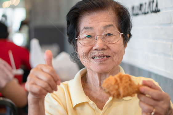 吃饭时间亚洲老年妇女正在餐厅吃炸鸡举起拇指她的笑容和看着快乐的老龄化社会概念退休后准备过着幸福的生活笑声午餐可口图片