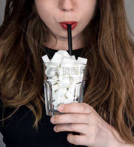 年轻女子用装满糖块的玻璃杯中黑色吸管喝水肖像垃圾食品不健康的饮食料中含糖过多营养概念特写食物饮料含糖过多营养概念苏打甜的活力图片