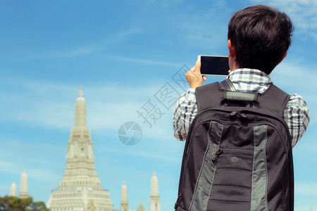 男人在泰国河上站着自拍旅行者拿着手机拍摄自己与泰国的WatArun一起微笑的照片男是背包黑色用智能手机拍照佛教徒河边地标图片