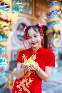 穿着红色传统青山装饰焦点的亚洲小可爱女孩在泰兰神庙举办新年庆典展示金钱袋以备新年盛会时使用重点旗袍愉快图片