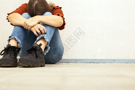 虐待郁闷年轻女子哭泣坐在空荡的墙边孤独悲伤和沮丧的女孩低着头保持图片