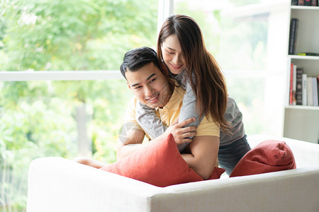 亚洲房间活的坐在沙发上快乐的一对情幸福侣当一个女人在客厅里爱着她男朋友笑微拥抱她男朋友在情人节浪漫的概念求婚和姻图片
