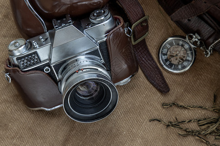 语气照片摄影机和棕色皮袋的顶端景象上面有围巾和口袋手表印在麻布背景上假日旅行概念设计镜片优质的图片