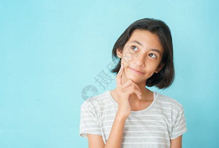 亚裔女孩在背景蓝色孤立与触摸下巴时带着笑容和快乐的脸高仰望着文本或广告的复制空间颜色或者学生图片