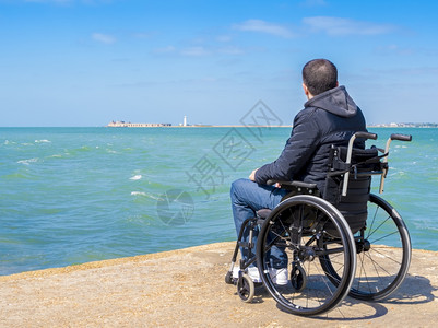 一种安全坐在轮椅上看海的残疾青年男子独身残疾人自然图片