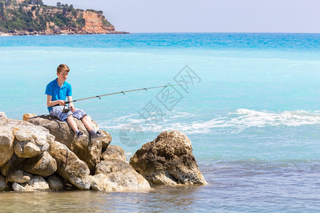 岛高加索少年男孩在海边和滩附近用棍子钓鱼岩石活动图片