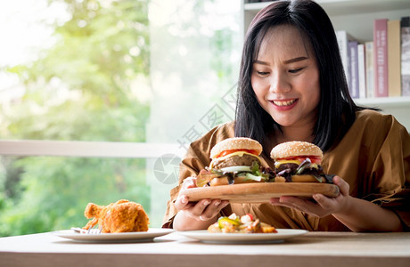 饥饿的超重女在分娩后将汉堡包放在木板上然后由送货员在家提供食物狂吃饮紊乱症BED概念与食用垃圾品放松成人蔬菜表示图片