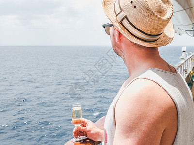成人游艇在蓝海浪背景下游轮露天甲板上握着美丽玻璃的帅哥侧观封闭式休闲和旅行概念露天甲板上握着玻璃的人ACONF19820饮料图片