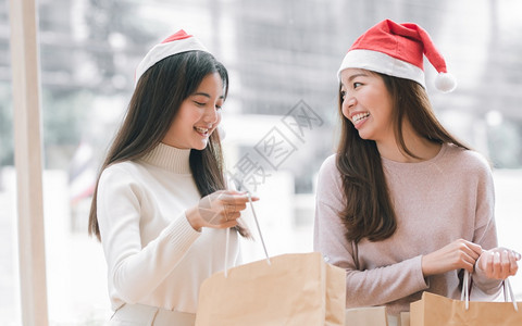 季节女士两名身戴圣塔帽的可爱妇女在圣诞节或新年庆祝活动期间持有纸袋和手晋升图片