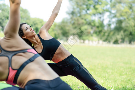两个美丽的年轻女青在公园做瑜伽锻炼在阳光明媚的一天在特制复空间年轻的练习肌肉图片