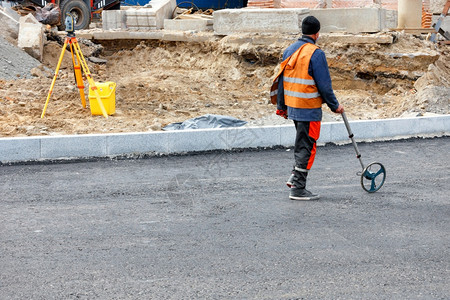 地形一名工程测量路途用一个计量车轮测道路距离确定在公路新段需要倒的沥青量A道路工人用电子计量车对工地进行计量A道路工人用电子计量背景图片