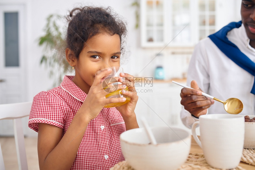 快乐的父亲和小女儿在早餐时喝果汁微笑的家人早上在厨房吃饭爸喂女孩关系很好父女在早餐时喝果汁健康好的坐着图片