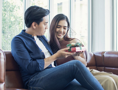 一个亚洲男人在客厅里坐的时候给女朋友送礼物妻子红色的浪漫图片