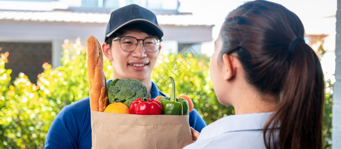 包裹妇女顾客站在家里接受一个食品水果蔬菜杂货袋由穿蓝制服的亚洲人送货员提供在科罗纳Coronavirus19流行期间提供服务航运图片