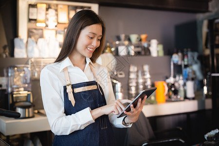 商业女员工接受在线客户的订单在网路用户的批发下亚洲女咖啡师在她的手中微笑着石板女雇员正在接受线上顾客的命令愉快在室内图片