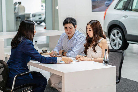 女售货员用过的亚裔销售员在决策前向一对夫妇客户解释销售合同然后在展厅购买新车经理图片