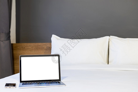 在旅馆卧室内背景工作和业余休闲以及度假旅行概念下的中用空白屏幕和智能电话在白色床上装饰的手提笔式电脑带有智能手机聪明的公司当代图片