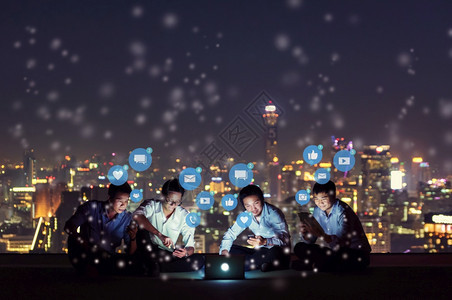 人们沟通利用智能手机平板电脑和笔记本工作或玩社交媒体的亚洲人群以及夜间有天线城市的高楼屋顶站点网社交络技术概念社交媒体和网络等媒图片