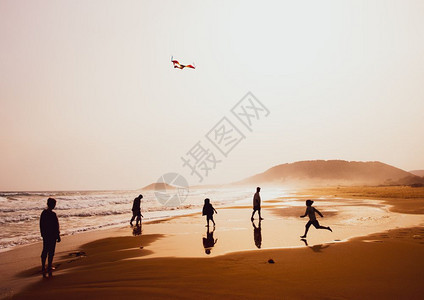 年轻的快乐人们在塞浦路斯卡帕西亚美丽的沙黄色金海滩上播放和风筝的人在大气中捕捉环形月光图片